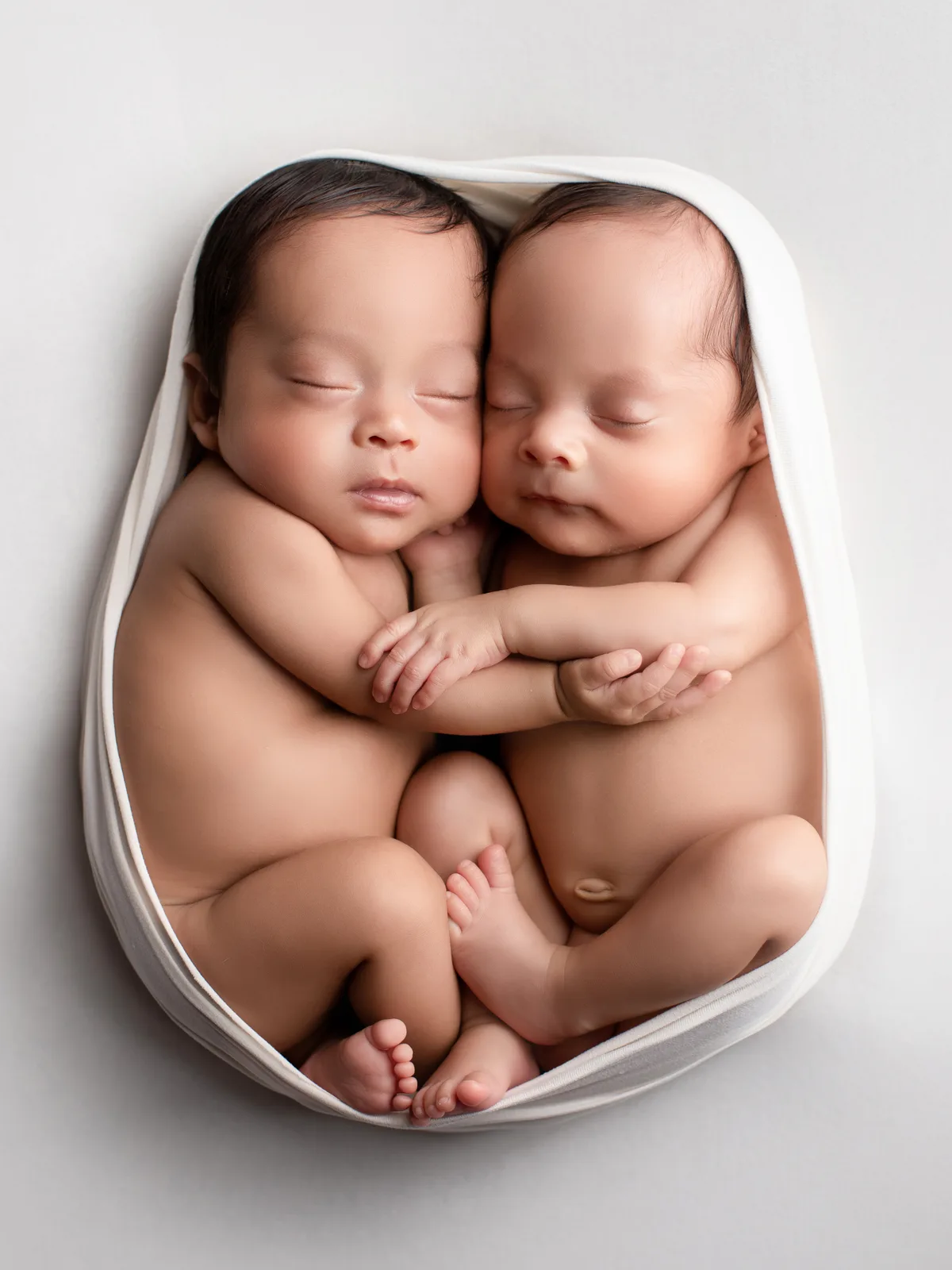 Gemelos recién nacidos dormidos y abrazados, envueltos juntos en una sesión newborn en Querétaro