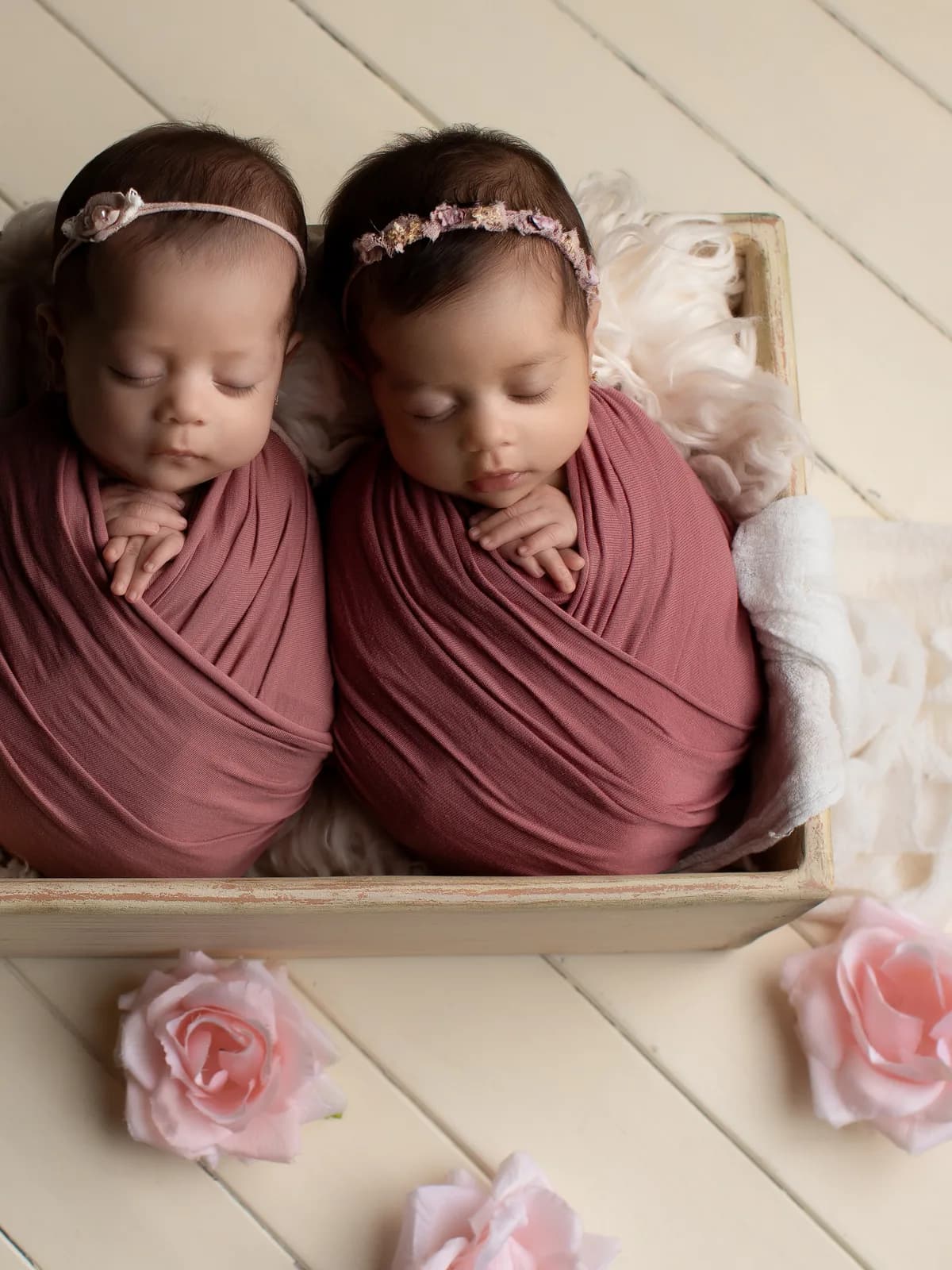Gemelas recién nacidas dormidas dentro de una canasta de madera, envueltas en mantas rosa durante su sesión newborn en Querétaro