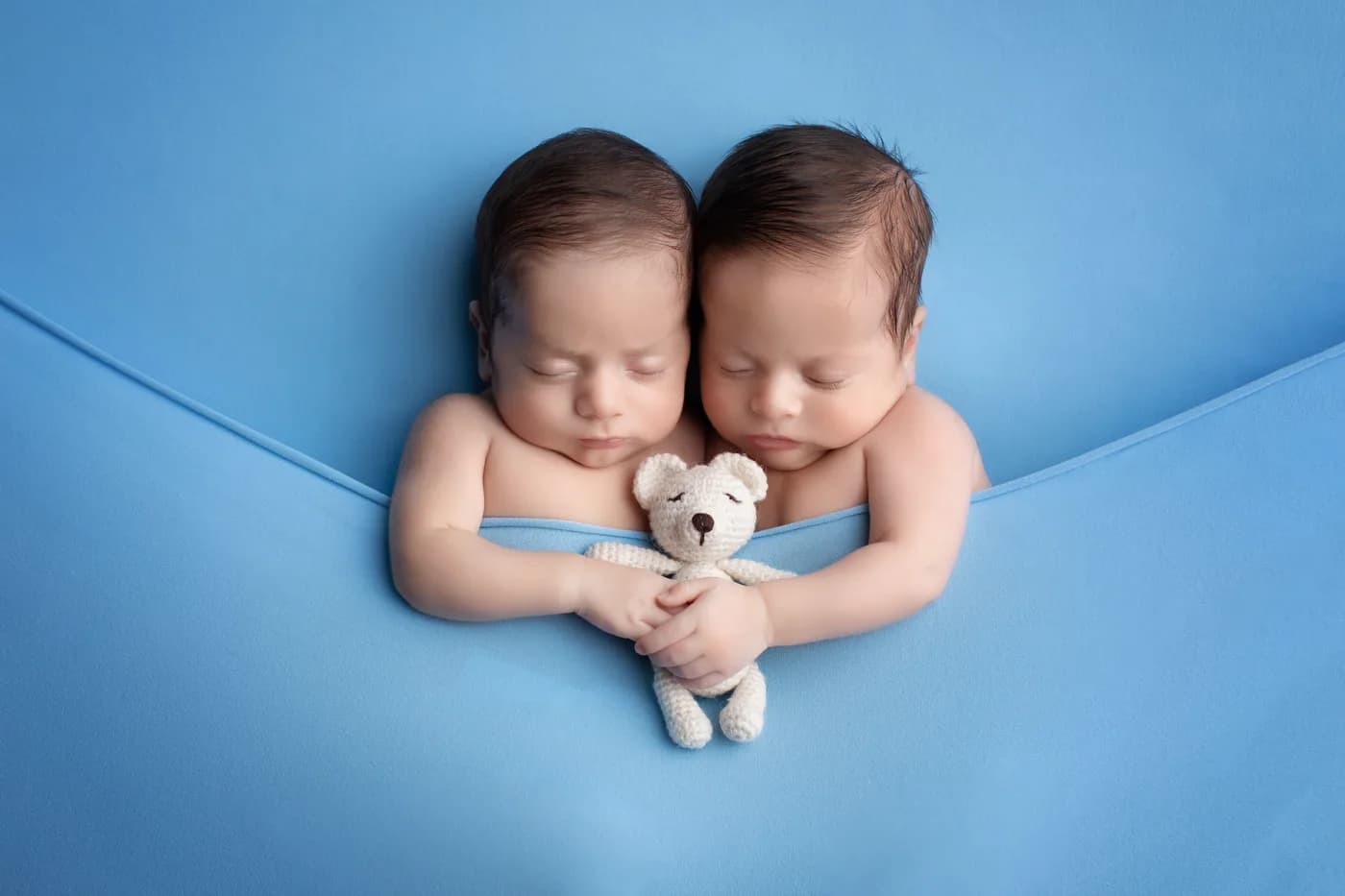 Gemelos recién nacidos dormidos abrazando un osito de peluche durante sesión newborn en Querétaro