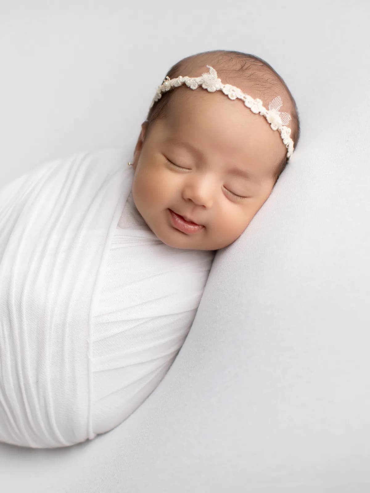 Recién nacida dormida y sonriente, envuelta en manta blanca durante sesión newborn en Bambuky, Querétaro